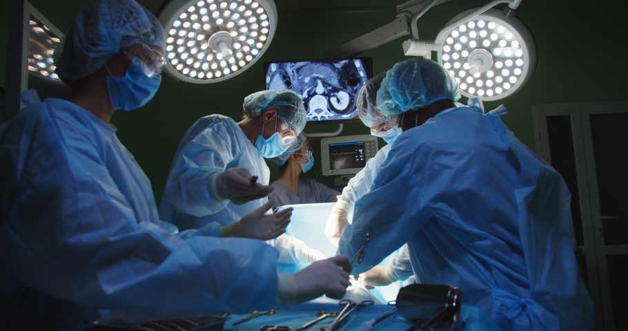 Group of mixed-races professional surgeons and nurses in uniform performing heart transplant surgery operation under bright lamps using medical instruments in operating room looking at screen Royalty-Free Stock Footage #1063329235