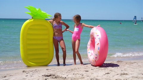 Two happy girls having fun on summer vacation. Adorable girls playing in the sea with inflatable mattress and inflatable ring