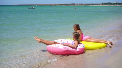 Two happy girls having fun on summer vacation. Adorable girls playing in the sea with inflatable mattress and inflatable ring