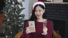 Young asian woman selfie video call online with friends and show glass in Christmas day on phone at home with social distancing, new normal, female video conference, communication and holiday concept.