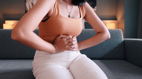 Woman having painful stomach ache sitting on sofa,Female suffering from abdominal pain,Period cramps,Hands squeezing belly,Stomach pain,Menstruation