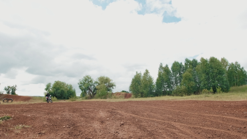 Portrait slowmo of man in helmet riding motorcycle on off-road track and stopping before camera