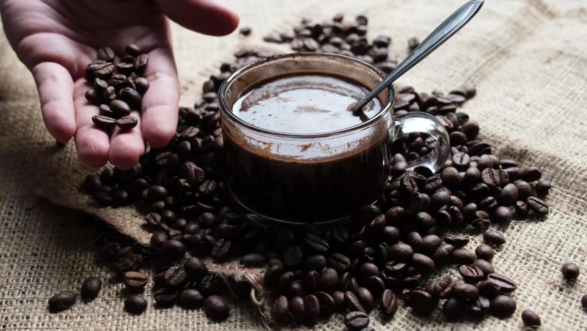 A man's hand was taking a coffee bean to contemplate next to a coffee cup with coffee beans all around. | Shutterstock HD Video #1063338988