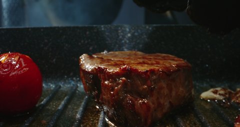 Chef preparing a delicious meal. Cooker frying pieces of juicy beef meat and tasty vegetables on grill. Steak grilled on professional kitchen - food art, food and drink 4k footage