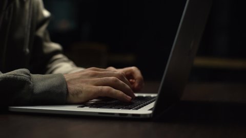 Close-up of unrecognizable hacker man stretching hands and starting to typing on laptop computer keyboard and breaking password. Freelancer using laptop working from home. Tracking shot in slow motion