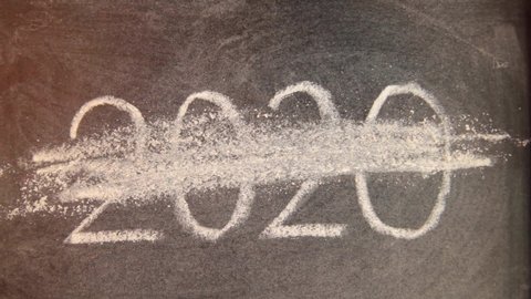 Human hand with annoyance crosses out chalk inscription 2020 on school blackboard