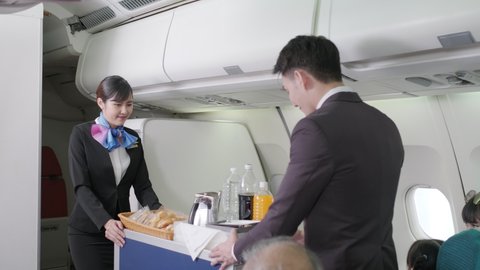 Flight attendants or stewardess are moving trolley and serving light snack, water and tea of coffee to passengers in the flight in economy class. Travel and relaxation concept.