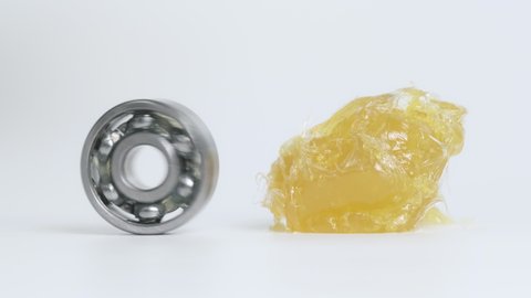 Ball-bearing spin beside yellow lithium grease (NLGI 2) and moving to grease isolated on white background . Wear and rust protection. Reduce friction. Engineering and industrial concept