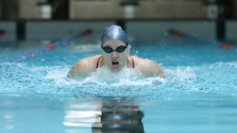 Athlete woman swims butterfly technique in indoor lap pool and preparing for olympic games. Front view video showing endurance, sport, professional swimming.