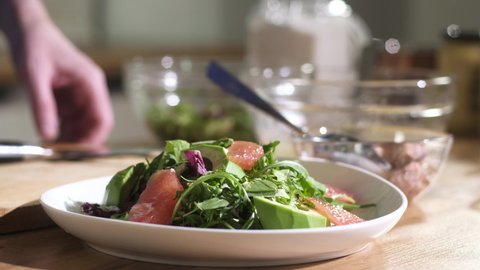Chef prepares diet lunch in kitchen. chef puts slices canned tuna on plate salad with arugula avocado grapefruit. Cooking delicious dish  vegetables and fruits. Healthy food vitamin for vegetarians
