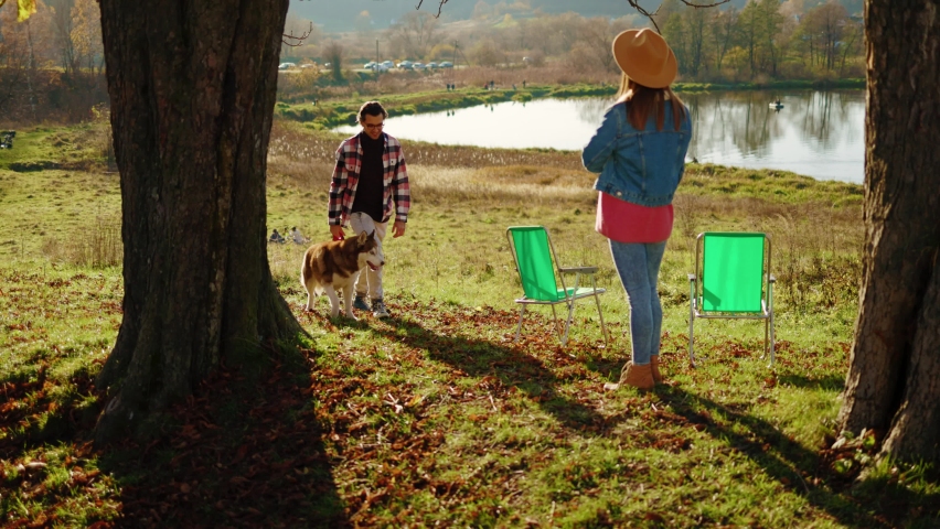 In autumn forest near lake man and woman met each other hug stand with dog at sunlight. Feel happy. Animal relaxed portrait cheerful. Close up. Slow motion