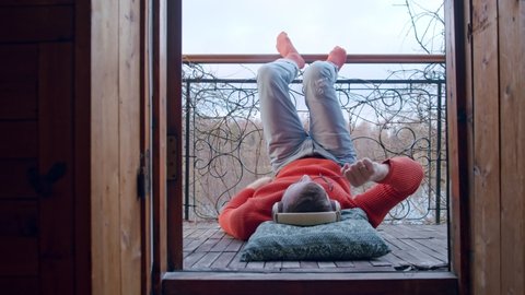 a man with headphones is dancing on his balcony lying on the floor with his feet up. Happy spending time during the pandemic and the second wave of coronavirus