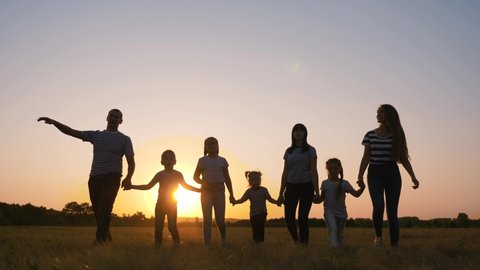 Happy big family in the Park at sunset. People on a walk have fun. Mom dad son and daughters walk together in the field. People holding hands, teamwork. Family trip on foot.