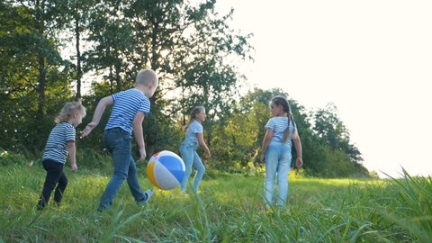A happy family of children run in a group to the Park and play with an inflatable ball. Kids kick and catch up with a colored ball. Girls and a boy in a team compete for a toy. Teamwork