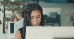 Portrait of young black business woman sitting in work space, chatting to discussing communicating by video call colleagues in office. Female looking at computer on online conference. 4K slow motion
