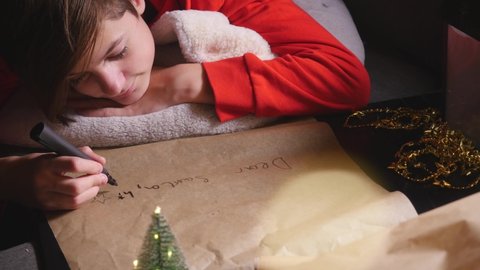 Teenage boy writing long letter to Santa at evening time. High angle view