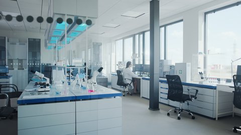Modern Medical Research Laboratory with Female Scientist Working at the Far Corner Desk. Scientific Lab with Technology Capable for Drugs and Vaccine Development, Full of High-Tech Equipment