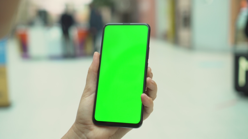 Shopping centre. Department store. Mall. Back view of brunette holding chroma key green screen smartphone watching content. Shopping online. Gadgets and contemporary people concept. | Shutterstock HD Video #1063360054