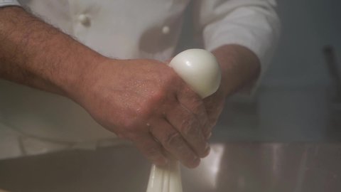 Italian chef dairy cheese production facility. Manual production, his hands takes white mozzarella from metal vat, crumples, makes burrata, squeezes, inflates ball. There steam from high temperature.