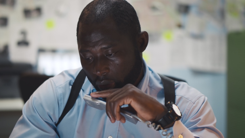 African young detective sitting at police department talking to colleague on phone. Portrait of black male cop having phone call with witness investigating burglary case in office Royalty-Free Stock Footage #1063363438