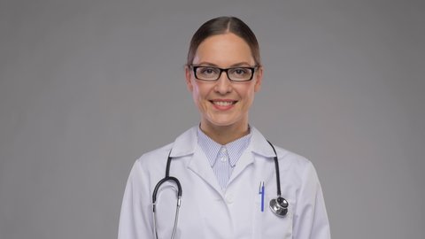 medicine, vision and healthcare concept - happy smiling female doctor in glasses and white coat over grey background