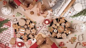 Kids is decorating a traditional gingerbread. Xmas flat lay video. Christmas and New Year holidays mood. Three children glaze a cookie. Top view of home table