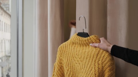 Seller's hand consultant gives a girl a yellow sweater in a fitting room in a clothing store