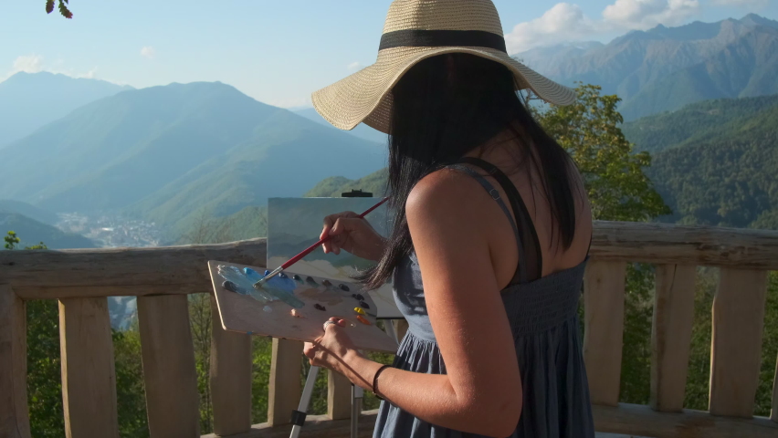 Female painter mixing oils on the palette to get the best colour. Creating artwork with mountain landscape en plein air