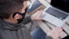Handsome man in face mask sitting outdoors in cafe and working on laptop. Man take salad. Quarantine. Covid-19 - Powered by Shutterstock - Get 15% off with code: PIKWIZARD15