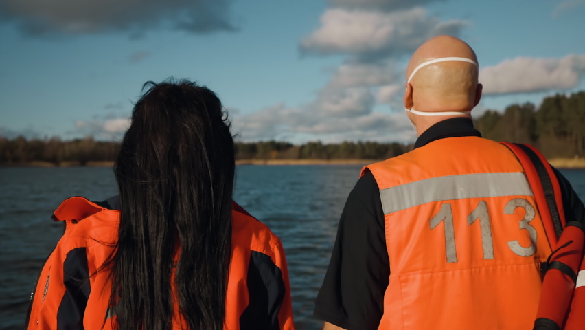 Two proud paramedics turn around near blue lake on sunny day