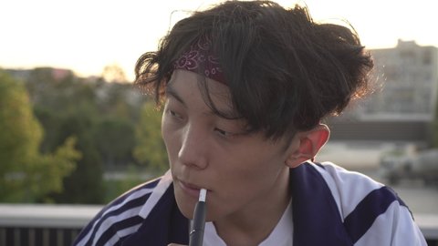 A young Asian man smokes an electronic cigarette with a tobacco heating system