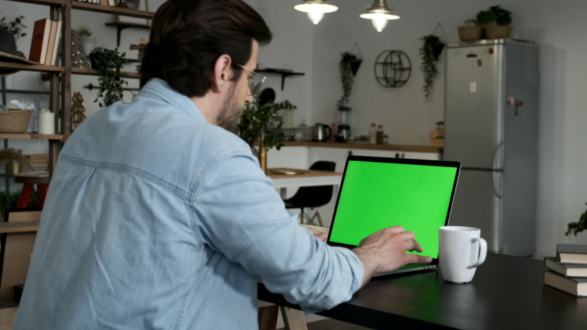 Over the Shoulder Shot of a Young Businessman Typing on Laptop with Green Mockup Screen While Working at Desk in the Office Royalty-Free Stock Footage #1063380112