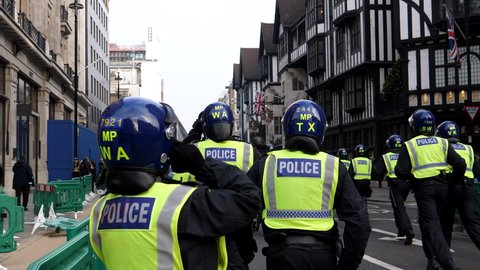LONDON, ENGLAND, UNITED KINGDOM - 28, NOVEMBER, 2020: Riot police officers with helmets running behind protest demonstration past Tudor style Liberty building in Great Marlborough Street in Soho.