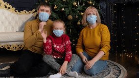Happy family is celebrating Christmas with their friends using video call. Parents and child in medical masks greeting their relatives on New year online.