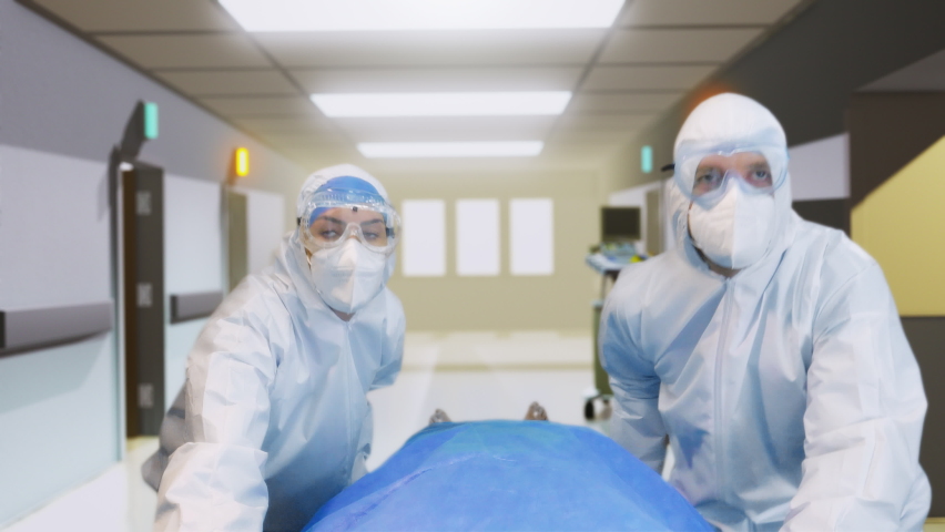 Emergency Covid: Doctors wearing White Coverall Move Seriously Infected Patient Lying on a Stretcher Through Hospital Corridors. Medical Staff in a Hurry Move Patient into Operating Room. 4k UHD. Royalty-Free Stock Footage #1063385086