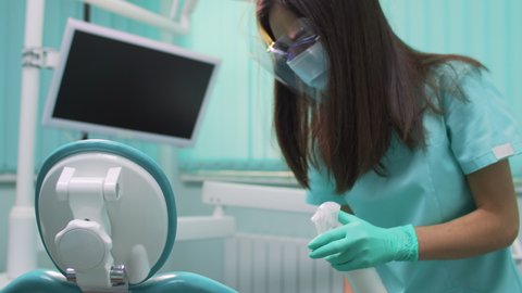 A nurse cleans and disinfects a chair in a dental office.