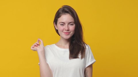 Secret smiling brunette young woman 20s in white t-shirt posing isolated on yellow color background studio. People lifestyle concept. Looking camera close her mouth lock and throw away key blinking
