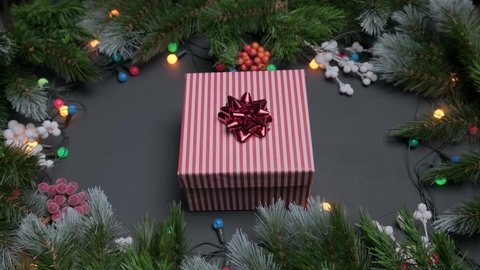 Men hands put desired gift on table and take it back, gift box with red bow on Christmas background, decorated with fir branches and bright colored garlands of lights. Gift for new year and Christmas.