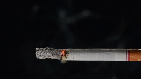 Lit and burning cigarette with smoke on black background