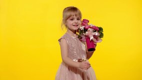 Young child girl with fashion makeup standing with bouquet of flowers isolated on yellow background. Friendly little blonde kid with flowers for mother. People emotions. 