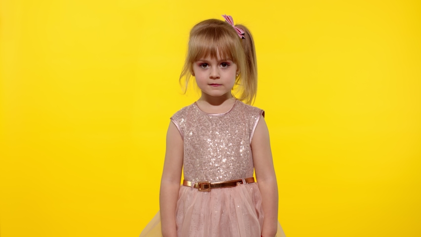 Irritated child girl in dress raising hands in questioning gesture why, what. Kid scolding with indignant expression, blaming in defeat. Yellow background studio. People emotions concept. Copy space Royalty-Free Stock Footage #1063391626