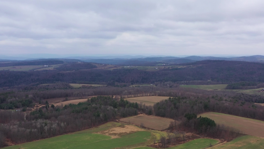 Aerial flyover beautiful Pennsylvania, USA countryside with hills in background and forest during cloudy sky.