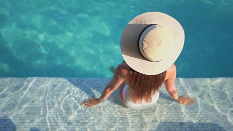 Woman In Swimsuit and Summer Hat Sitting on a Pool Edge, High Angle View. Dreamy Scenery and Holiday Memory Concept, Full Frame