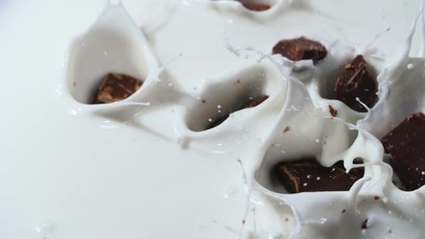 Chocolate slices fall into the white milk. Close-up shot. Slow motion.