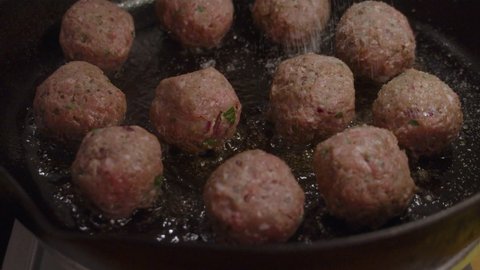 Adding spice on top of fried meatballs inside hot frying pan with boiling cooking oil. Slow motion shot.