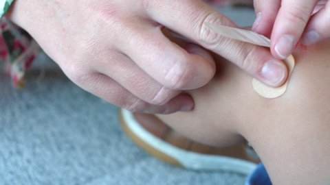 Close Up Mother's Hand putting Adhesive Bandage on Child's Knee Wound.
