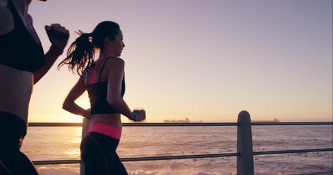 Two athletic woman running outdoors in slow motion on promenade at sunset near ocean enjoying evening run RED DRAGON