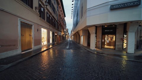 Rome , Italy - 04 18 2020: Dolly shot moving between shops, on narrow Via del Corso alley, dark, rainy evening, in Rome - Coronavirus Quarantine