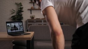 Back view of fit man doing cursty lunges with help of mixed race woman - online fitness trainer. Close-up of laptop showing streaming video of intense workout, sport exercises at home during lockdown