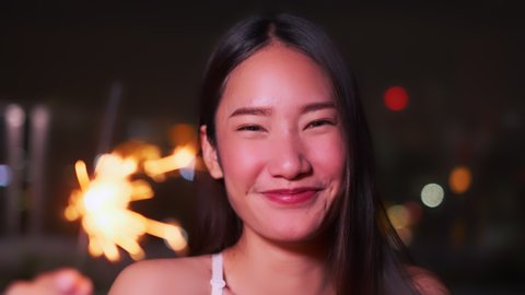 Young asian woman with sparklers is dancing and celebrating a new year. Fireworks, bengal lights in slow motion. Having fun at rooftop in the city.close up sparklers portrait low light.